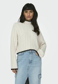 Beige ribbed sweater with a high neck, black trim at the hem and cuffs, paired with a blue denim skirt featuring a front slit.