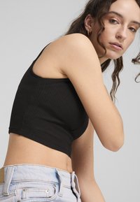 Zwarte geribbelde crop top met dunne bandjes, met een aansluitend ontwerp. Draagt bij lichte blauwe denim jeans.