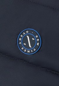 Marinblå kviltad tyg med en cirkulär logotyp med blå accenter och vit text. Logotypen inkluderar "AHEAD" och "NEW TIMERS" med ett stiliserat tecken.
