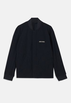 Marineblauwe jas van katoen, met een ronde kraag, drukknoopsluiting en twee grote, ronde zakken. Minimale branding aanwezig.