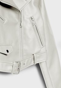 Veste en simili cuir gris clair avec une fermeture éclair diagonale, des poches zippées et une taille ceinturée avec des accents en métal argenté.