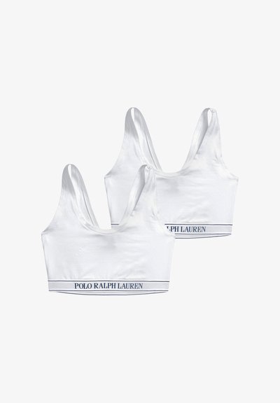 Deux brassières de sport blanches avec des bretelles larges et des bandes élastiques portant le texte "POLO RALPH LAUREN" en bleu marine sur fond blanc.