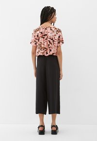 Gemustertes pinkes Oberteil mit kurzen Ärmeln und rundem Ausschnitt, kombiniert mit schwarzen, knöchellangen Hosen und klobigen schwarzen Sandalen.