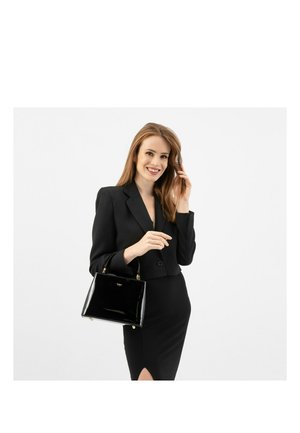 Schwarze Patentleder-Handtasche mit rechteckiger Form, goldener Hardware und kleinem Logo. Das Modell trägt einen figurbetonten schwarzen Blazer und ein Kleid.