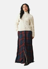 Cream cable-knit turtleneck sweater paired with a long plaid skirt in burgundy, navy, and green, featuring front buttons and side slits.