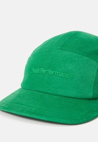 Green corduroy cap with a flat brim and stitched text "PeakPerformance" on the front panel. Textured fabric with vertical lines.