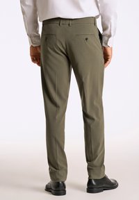 Olijfgroene op maat gemaakte broek met een gladde textuur, voorzien van twee achterzakken met zwarte knopen en een recht gesneden ontwerp, gedragen met zwarte schoenen.