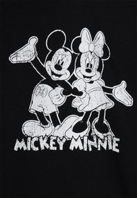 Topolino e Minnie Mouse in piedi fianco a fianco, sorridenti con le braccia aperte, stampa vintage bianca su sfondo nero con i nomi sottostanti.