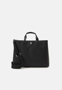 Sac fourre-tout en cuir noir avec des poignées doubles, une bandoulière amovible, un logo en argent brillant, une texture lisse et une forme structurée.