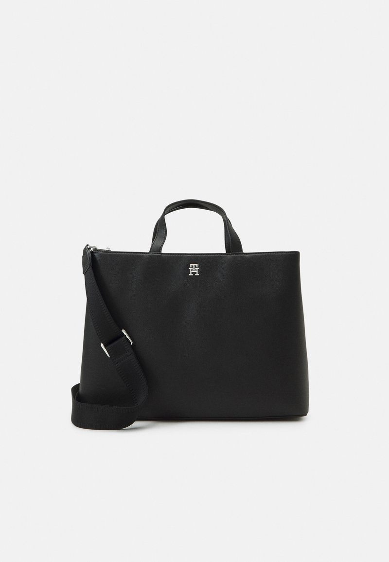 Sac fourre-tout en cuir noir avec des poignées doubles, une bandoulière amovible, un logo en argent brillant, une texture lisse et une forme structurée.