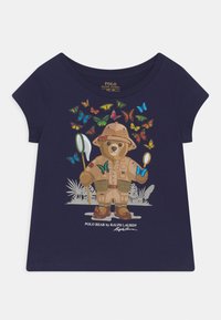 Tmavě modré tričko s kresleným medvědem v safari outfitu, obklopeným barevnými motýly. Krátké rukávy a kulatý výstřih.