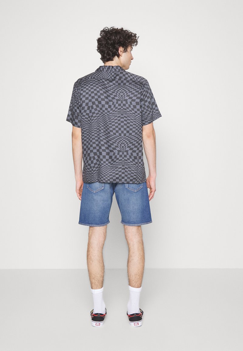 Camisa de cuadros negra de manga corta con un patrón en espiral, combinada con pantalones cortos de mezclilla, calcetines blancos y zapatillas negras y rojas.