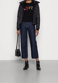 Černá prošívaná bunda přes černý svetřík s barevným nápisem "LOVE", kombinovaná s tmavě modrými zkrácenými džínami a černými kotníkovými botami. Černá kabelka.