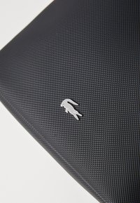 Črn teksturiran material z argentinskim krokodiljim logotipom v enem kotu, ki prikazuje sodoben dizajn in trpežno površino.