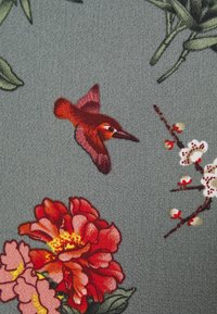 Textil floral con grandes peonías rojas y rosas, flores blancas y un colibrí marrón y rojo volando sobre un fondo gris texturizado.