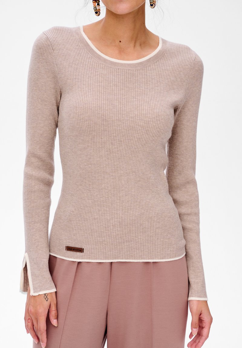 Beige geribbelde langwerpige top met crèmekleurige afwerking bij de halslijn en manchet. Beschikt over een klein bruin label aan de zoom.