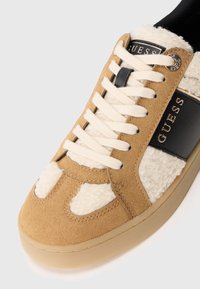 Sneaker in suede color tan con dettagli in ecopelle di shearling crema, striscia in pelle nera e lacci bianchi. Suola in gomma e dettaglio logo dorato.