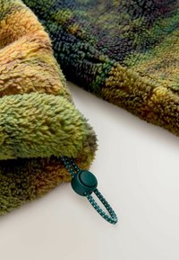 Couverture en polaire aux tons verts et jaunes variés, dotée d'une surface texturée et d'un cordon de serrage vert avec un taquet en plastique.