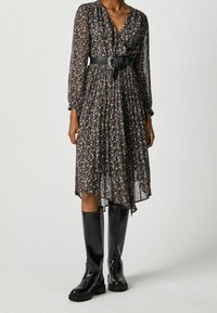 Svart blommig klänning med långa ärmar, v-ringning, åtsittande midja och lager-på-lager kjol, matchad med knähöga, glansiga svarta stövlar.