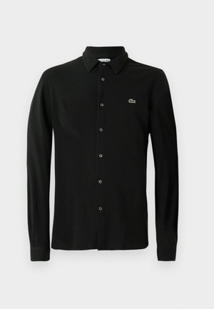 Polo de manga larga negro, hecho de material suave, con botones en la parte delantera y un pequeño logo de cocodrilo verde en el lado izquierdo del pecho.