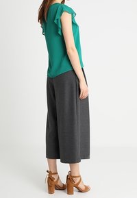 Blusa turquesa con mangas con volantes, combinada con culottes grises de talle alto y sandalias de tacón bloque color beige. Tejido texturizado.