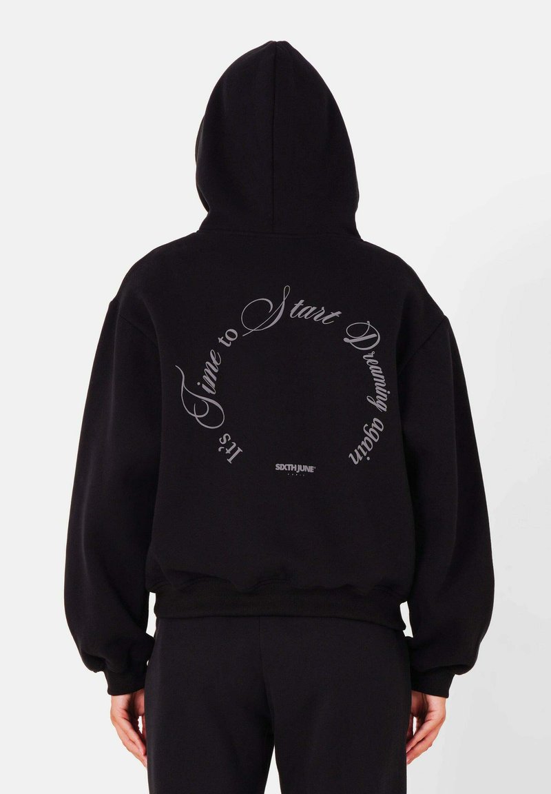 Zwarte hoodie met een cirkelvormige tekstgrafiek in het wit op de achterkant, met de frase "Het is tijd om te beginnen dromen" en logo-detail.