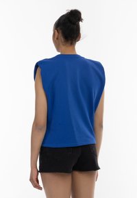 Blå ærmeløs top lavet af bomuld, med en rund halsudsk�æring og struktureret skulderdesign, parret med sorte denimshorts.