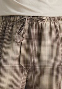 Checkered pajama pants in brown and cream, featuring an elastic waistband with a drawstring and subtle texture in soft fabric.
