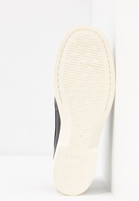 Semelle d'une chaussure noire avec une semelle extérieure blanche, une bande de roulement texturée, le logo "Camper" et une étiquette "Extralight", présentée debout sur un fond blanc.