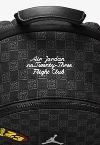 Must musta, millel on tekstureeritud kangas õrnalt 23 mustriga, valged tikitud tähed ja musta logoga plekke all.