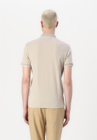 Beige piké skjorte med korte ermer, kontrasterende krage, glatt tekstur og en avslappet passform. Brukt med lyse bukser.