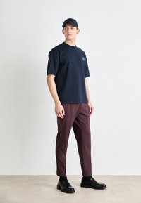 Ναυτικό μπλουζάκι από βαμβάκι, κοντά μανίκια, στρογγυλή λαιμόκοψη; μπορντό παντελόνι σε χαλαρή γραμμή; μαύρα παπούτσια με λεία φινίρισμα.