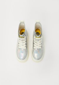 Srebrne sneakersy typu high-top z holograficznym połyskiem, białymi sznurowadłami, grubą podeszwą i żółtą metką wewnętrzną. Gładki materiał syntetyczny.