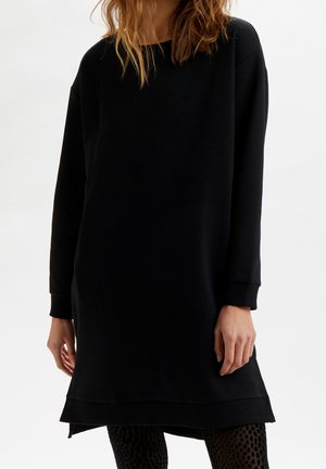 Robe sweatshirt noire à manches longues, coupe décontractée, encolure ronde et ourlet arrière légèrement plus long. Matière en coton doux. Leggings texturés.