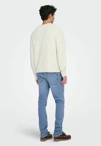 Pull en tricot crème clair à col rond, associé à un jean bleu clair. La tenue est complétée par des chaussures à lacets marron foncé.