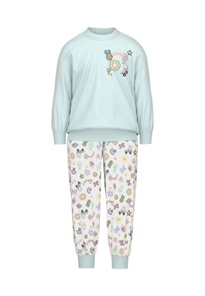 Minzgrüner Pullover mit verspielten Grafiken; gemusterte cremefarbene Hose mit bunten Illustrationen von Blumen, Sonnen und niedlichen Formen.