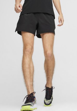 Sorte sporty shorts med en glat overflade, der har to sidelommer og en tætsiddende pasform. Sammen med farverige løbesko.