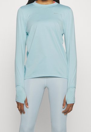 Persoon draagt lichtblauw langwerpig actief shirt met duimgaten en bijpassende legging tegen een effen achtergrond.