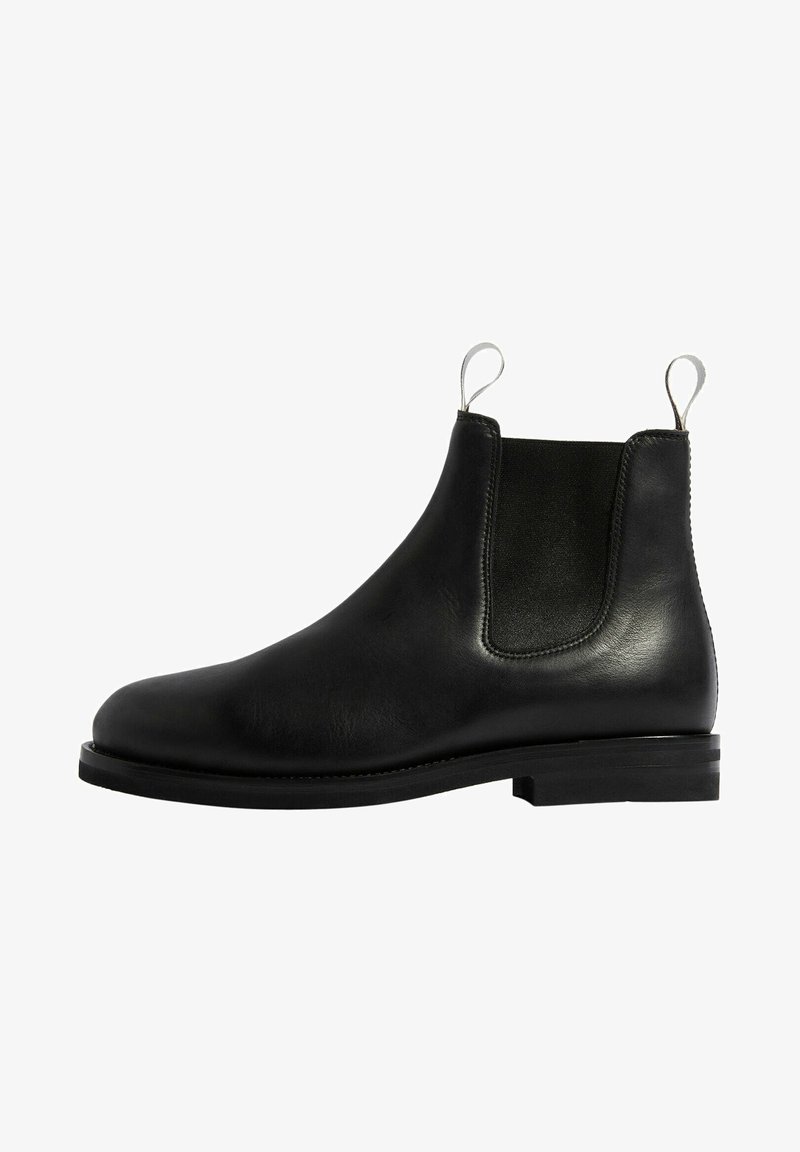 Bota Chelsea de cuero negro con paneles laterales elásticos, punta redondeada y suela de goma plana. Incluye lengüetas para facilitar su uso.