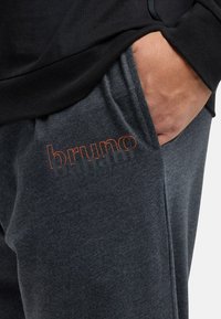 Mørkegrå sweatpants med orange broderi af mærkenavnet. Blødt stof med en afslappet pasform, der har en sidelomme og elastisk talje.