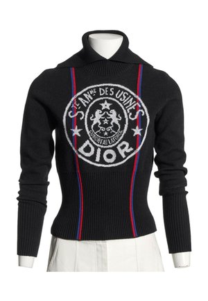 Pull côtelé noir à manches longues avec col montant, rayures verticales rouges et bleues, et logo Dior circulaire blanc sur le devant.