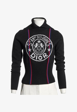 Pull côtelé noir à manches longues avec col montant, rayures verticales rouges et bleues, et logo Dior circulaire blanc sur le devant.