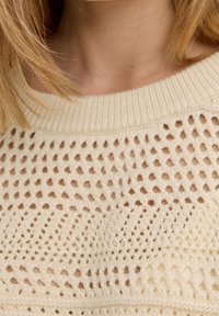 Pull tricoté couleur crème avec un motif ajouré, col côtelé et détails texturés, présentant un design léger et aéré.