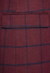 Bordowa tkanina o teksturowanym splotem, z niebiesko-czarnym wzorem w kratę. Widoczna jest pojedyncza kieszeń na piersi, co podkreśla design.