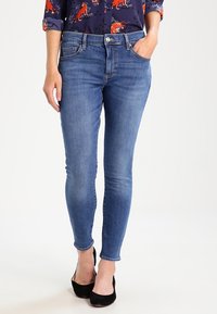 Smal blå jeans i denim med klassisk femficksdesign. Har subtila slitningar och midjeband i midjan. Mjuk textur och lätt stretch.