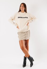 Maglione a maglia crema con logo "PATRIZIA PEPE", abbinato a una gonna a quadri beige e stivaletti neri con tacco spesso.