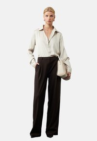 Lichtbeige overhemd met knopen en een zachte textuur, zwarte hoge taille broek en een lichtbeige gestructureerde handtas.