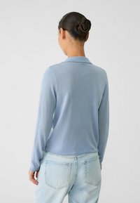 Hellblaues Langarm-Polohemd mit Kragen, glatter Textur und leicht lockerer Passform, kombiniert mit hellen Jeans.