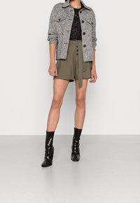 Veste grise à motif avec deux poches avant, top en dentelle noire, shorts olive à nouer devant et bottines noires en vernis.