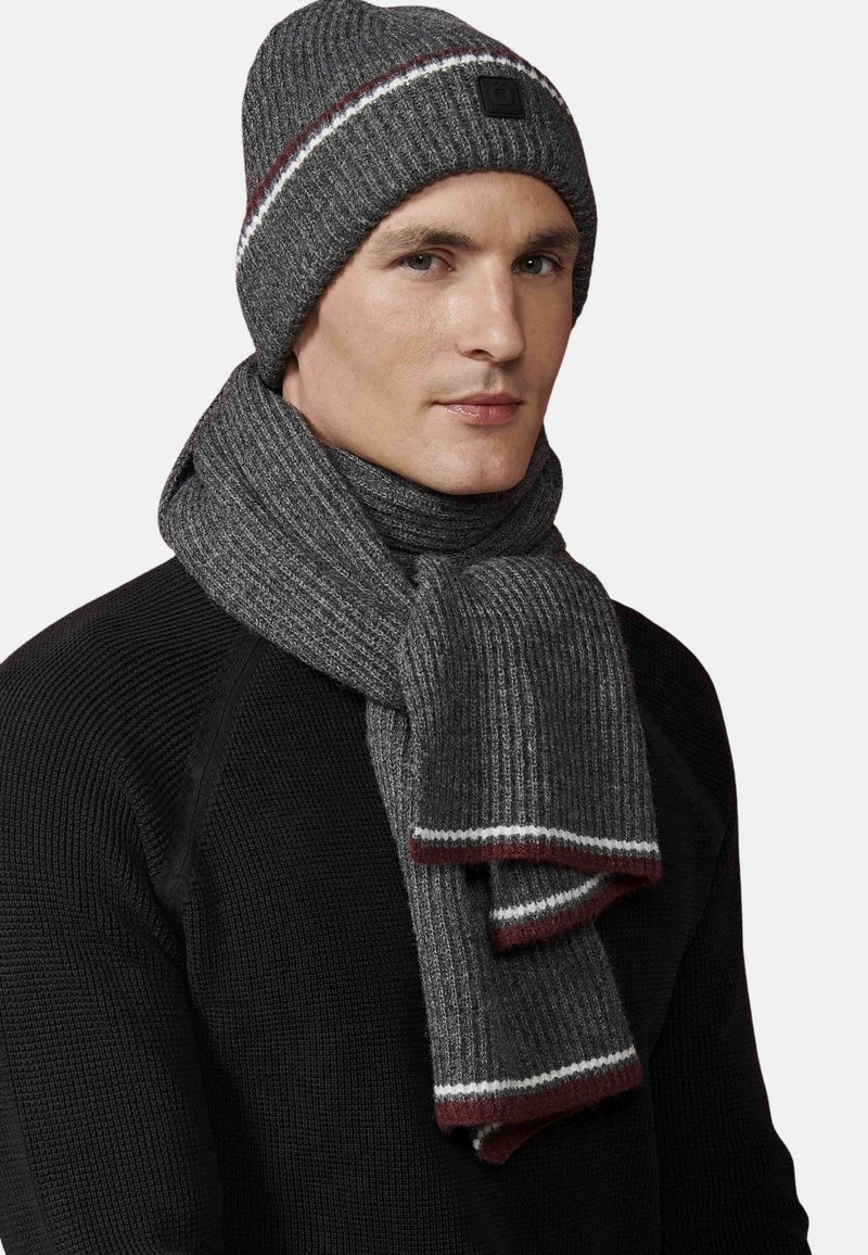 Szary sweter beanie z czerwonymi i białymi paskami, w komplecie z dopasowanym szarym szalikiem w prążki. Obie rzeczy mają miękką teksturę i zorganizowany design.